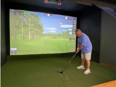 interior golf simulator bay with left handed golfer ready to swing