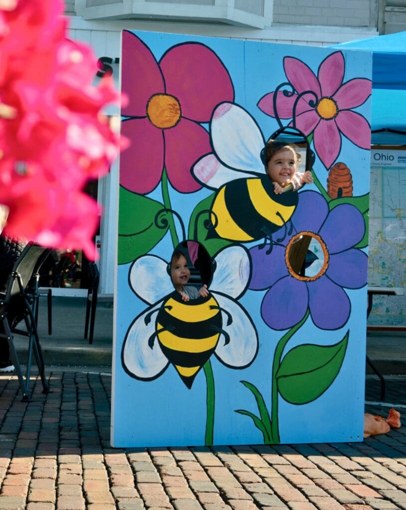 two kinds standing in the cut out images of two bees getting their photo taken