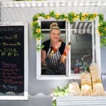 A local vendor leans out the window of her food truck with shish kabobs in hand.