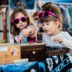 Two young girls in sunglasses look through items for sale at a vendor's booth