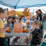 A group of children sits at a table painting pumpkins.