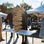 A group of four people plays oversized Jenga with beers in hand.
