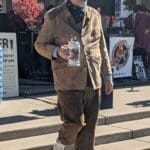 A man dressed in German attire walks down some stairs with a beer stein in hand.