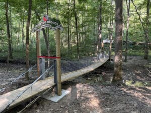 A swinging bridge stretches across a creek, with a sign that reads, "Hueston Woods Nature Preserve Old-Growth Beech-Maple Forest