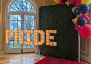 "PRIDE" lighted marquee letters in front of a beautiful window and selfie station